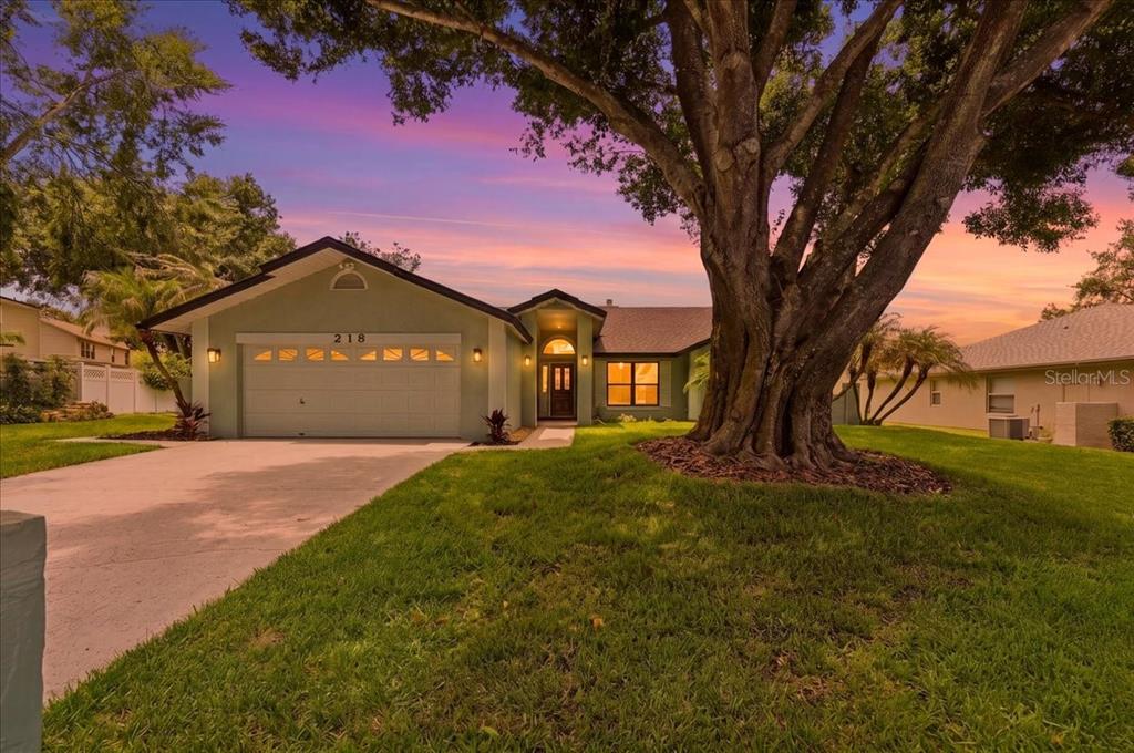 A single-story house with a green exterior, a two-car garage, and a large front tree — 218 LAKE HARTRIDGE DRIVE NW, WINTER HAVEN, FL