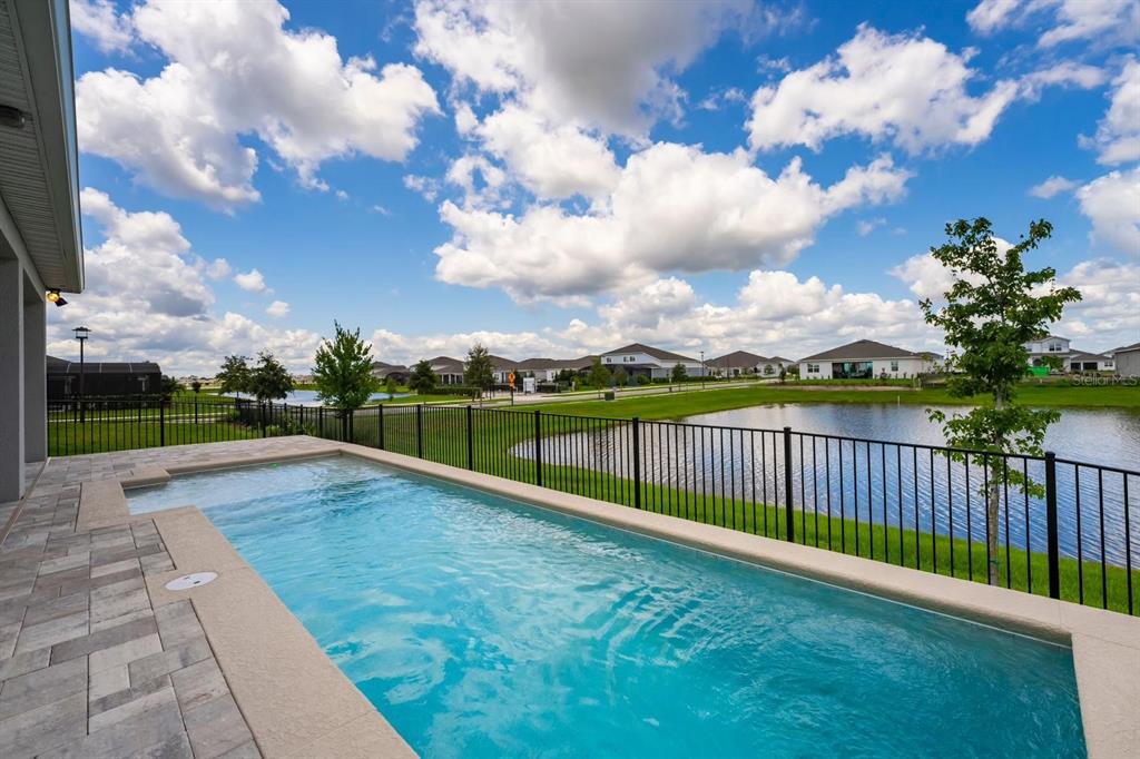 A rectangular swimming pool sits on a patio overlooking a pond and suburban houses — 13864 DESTIN BEACH LANE, ORLANDO, FL