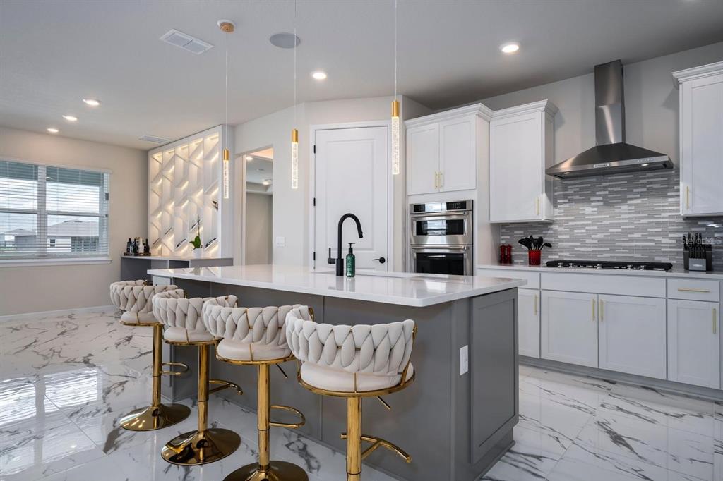 A modern kitchen features a gray island, white cabinetry, gold accents, and marble-patterned flooring — 13864 DESTIN BEACH LANE, ORLANDO, FL