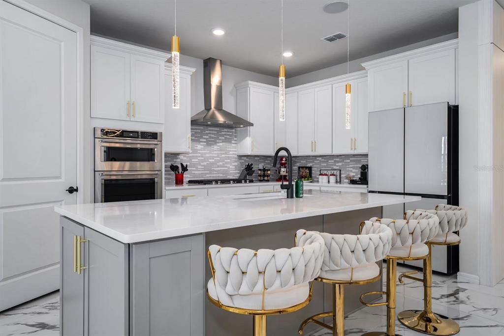 A modern kitchen features white cabinets, a gray island with bar stools, and stainless steel appliances — 13864 DESTIN BEACH LANE, ORLANDO, FL