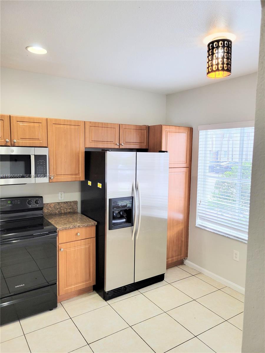 A kitchen features light wood cabinets, stainless steel appliances, and beige tile flooring — 8263 SW 27th St # 102, Miramar FL 33025, MIRAMAR, FL