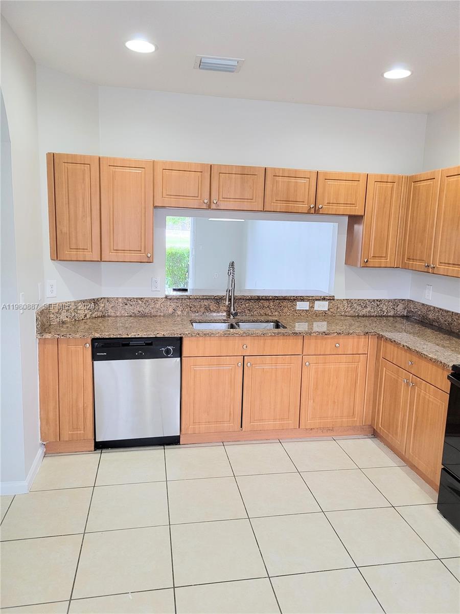 A kitchen features light wood cabinets, granite countertops, a stainless steel dishwasher, and tile flooring — 8263 SW 27th St # 102, Miramar FL 33025, MIRAMAR, FL
