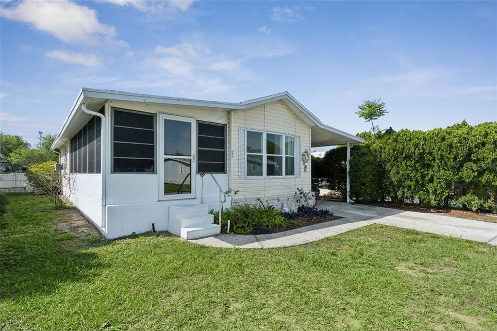A single-story mobile home features a screened-in porch, white siding, and an attached carport — 50989 HIGHWAY 27 UNIT 21, DAVENPORT, FL