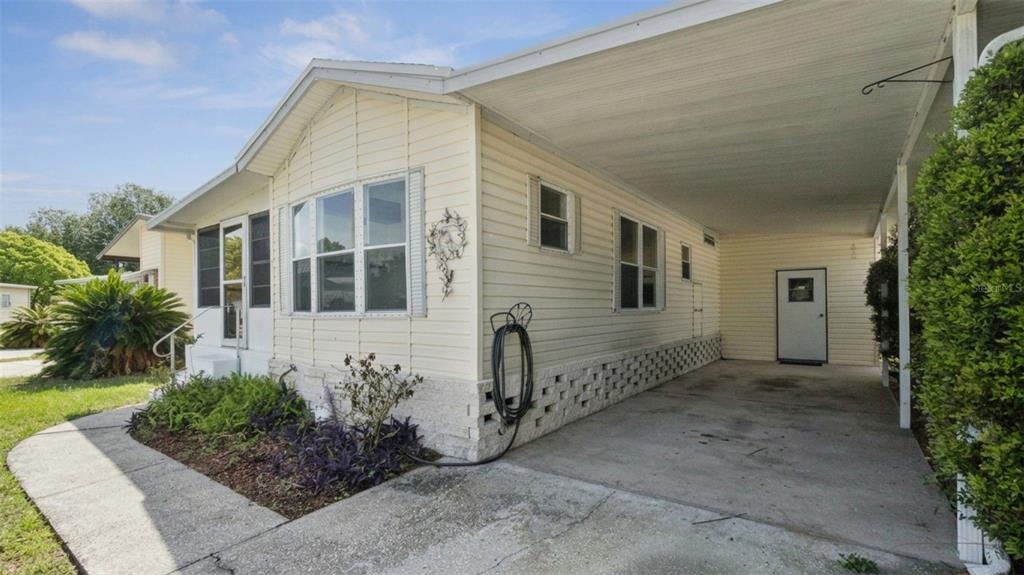 A light-colored mobile home features a side carport, a concrete driveway, and a small garden — 50989 HIGHWAY 27 UNIT 21, DAVENPORT, FL