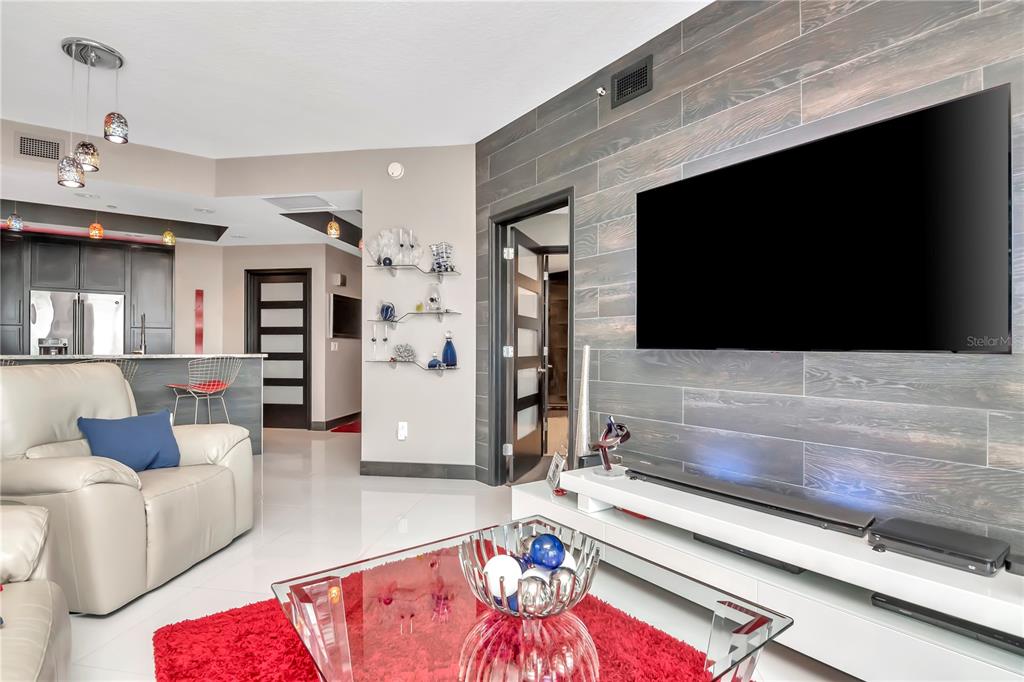 A modern living room features a wood-paneled accent wall, a large television, and white flooring — 449 S 12TH STREET UNIT 1006, TAMPA, FL