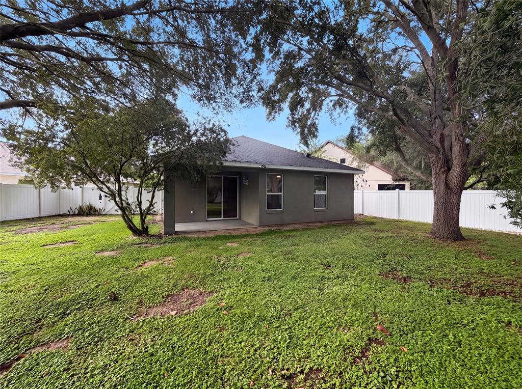 The backyard of a house features a covered patio, a lawn, and large shade trees — 33450 IRONGATE DRIVE, LEESBURG, FL