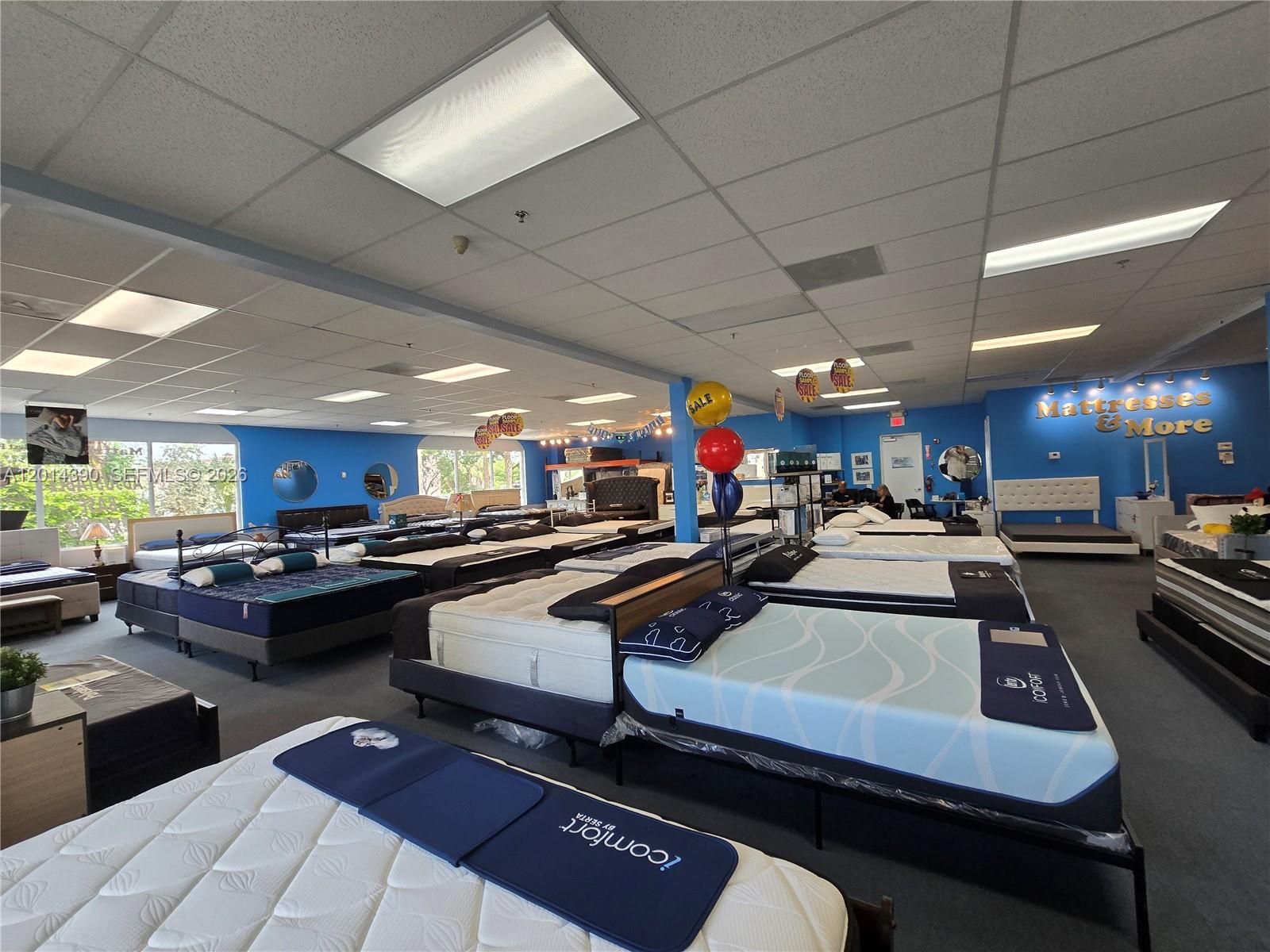 A mattress store showroom features multiple beds displayed on a carpeted floor under drop ceilings — 100 N State Road 7 # 102, Margate FL 33063, MARGATE, FL