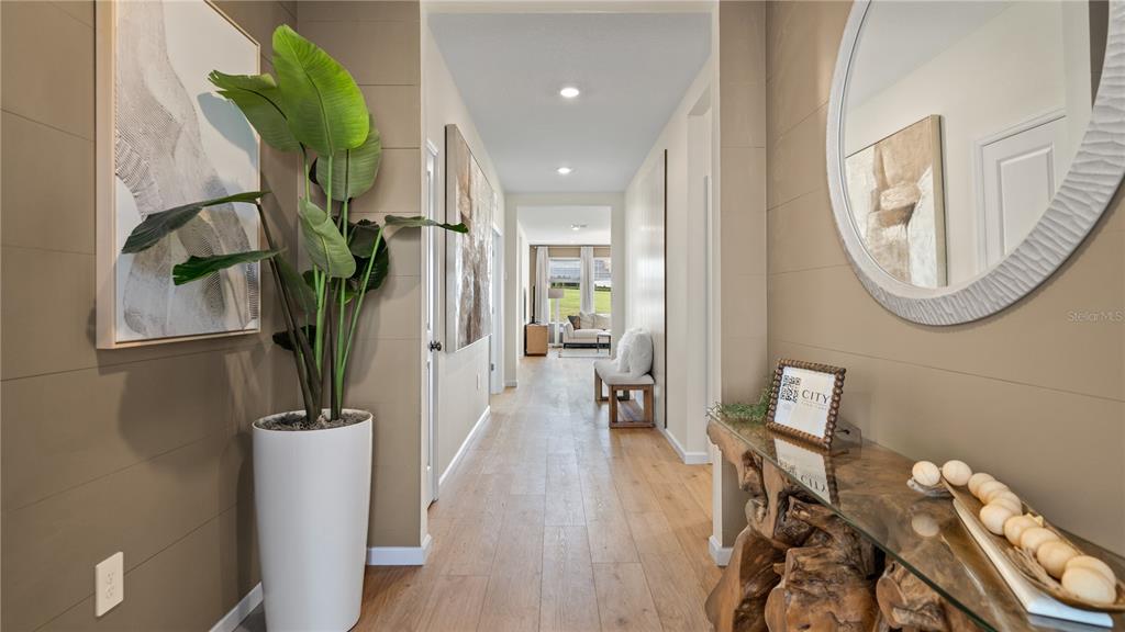 A hallway with light wood floors, a tall potted plant, and a rustic console table — 2692 MERCY CIRCLE, CLERMONT, FL