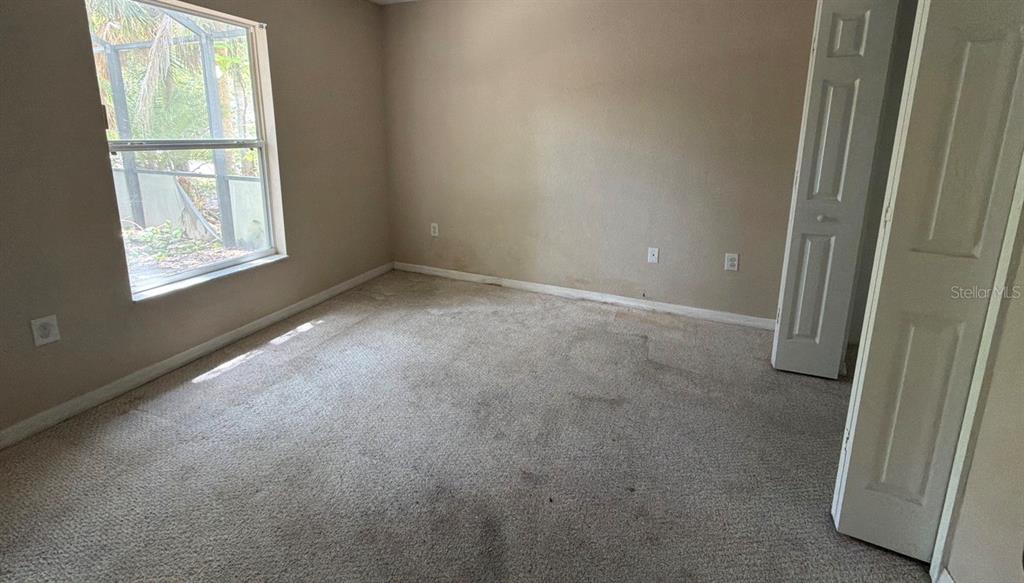 An empty bedroom with yellow walls, beige carpet, a ceiling fan, and a walk-in closet — 1365 BLAISDELL STREET, PORT CHARLOTTE, FL