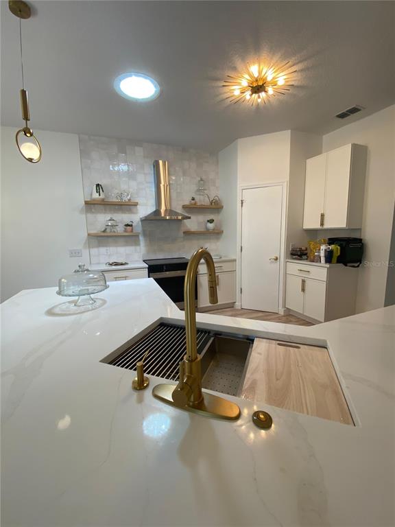 A modern kitchen features a white quartz island with a gold faucet and open shelving — 176 CAPE FLORIDA DRIVE, KISSIMMEE, FL
