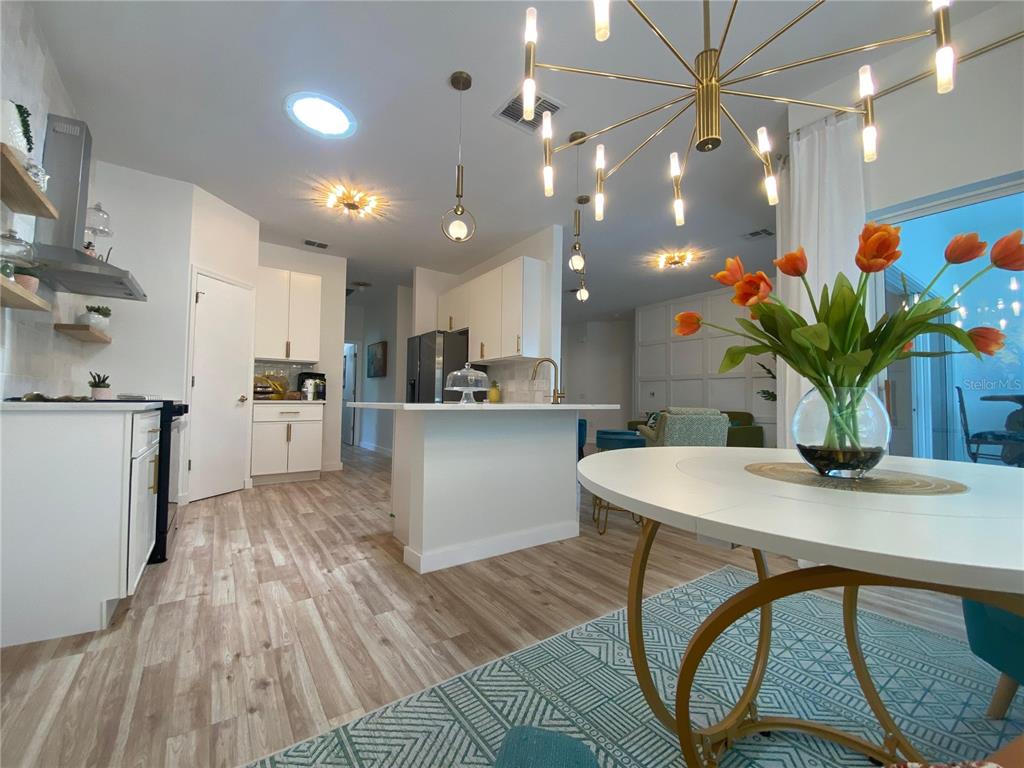 A modern kitchen and dining area feature white cabinets, a central island, and gold lighting — 176 CAPE FLORIDA DRIVE, KISSIMMEE, FL