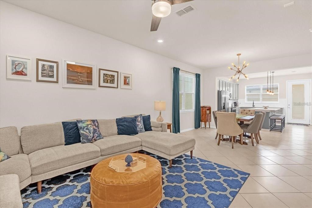 A living room with a sectional sofa and blue rug opens into a dining area — 5090 CASPIAN STREET, ST CLOUD, FL