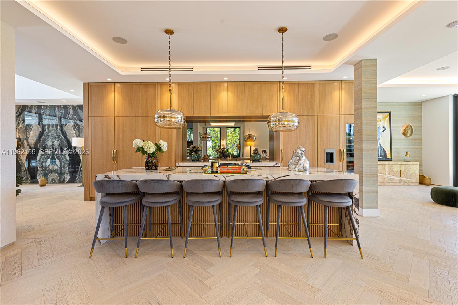 A modern kitchen features a marble-topped island with six grey stools and light wood cabinetry — 2499 N Meridian Ave, Miami Beach FL 33140, MIAMI BEACH, FL