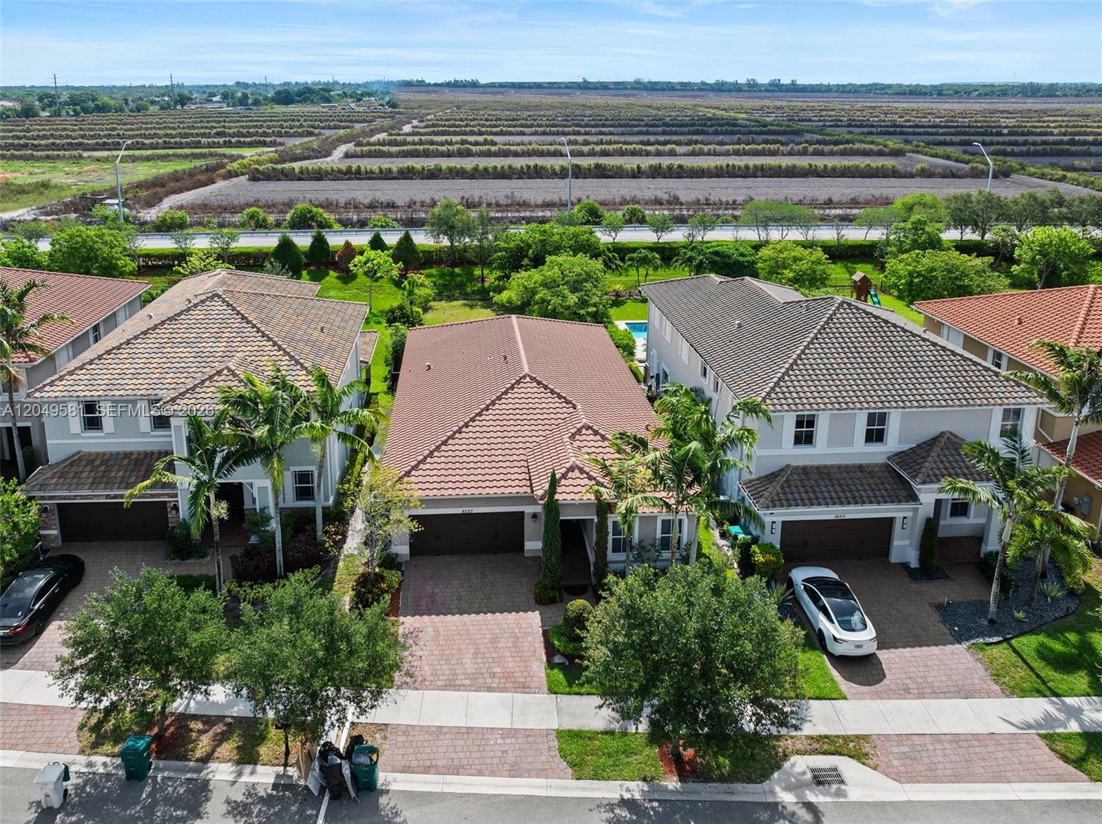 An aerial view shows three suburban houses with tiled roofs and driveways near a field — 8530 Miralago Way, Parkland FL 33076, PARKLAND, FL