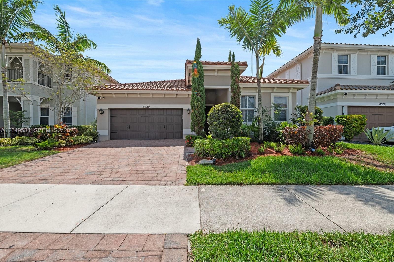 A single-story suburban house features a brick driveway, a two-car garage, and palm trees — 8530 Miralago Way, Parkland FL 33076, PARKLAND, FL