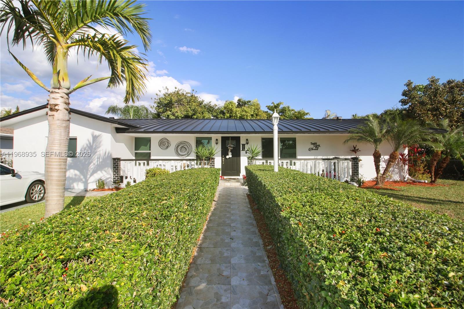 A white single-story house features a black metal roof, a central entrance, and manicured hedges — 16323 SW 103rd Pl, Miami FL 33157, MIAMI, FL
