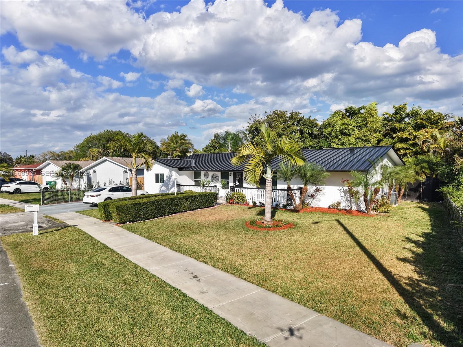 A white single-story house with a black metal roof sits behind a manicured lawn — 16323 SW 103rd Pl, Miami FL 33157, MIAMI, FL