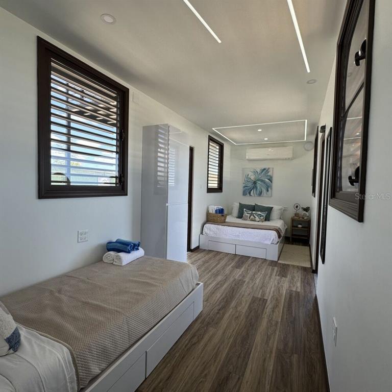 A bedroom with wood-look flooring, two beds, a white wardrobe, and a wall-mounted air conditioner — SR 545 km 1.5 SECTOR GABIA HACIENDAS DEL SUR TENNIS CLUB, SANTA ISABEL, PR