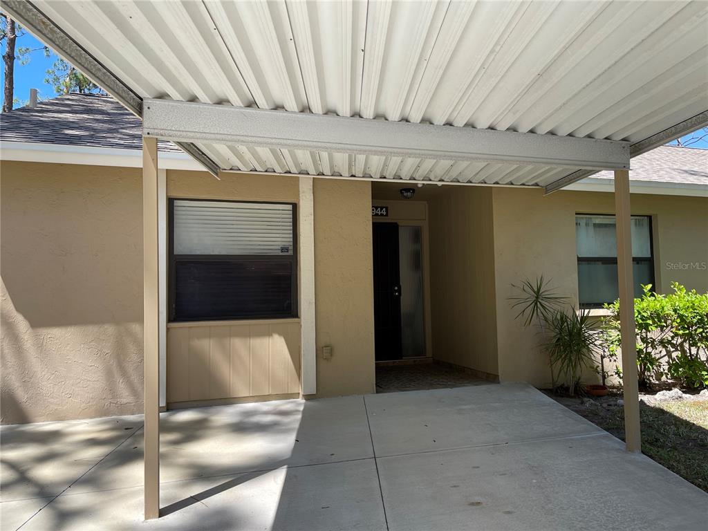 A beige house exterior features a concrete carport and a covered front entryway — 4944 VILLAGE GARDENS DRIVE UNIT 151, SARASOTA, FL