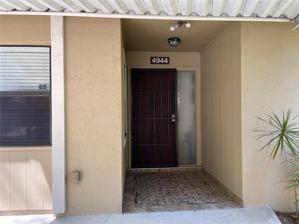 The exterior entrance features a security screen door, a tiled porch, and a house number — 4944 VILLAGE GARDENS DRIVE UNIT 151, SARASOTA, FL