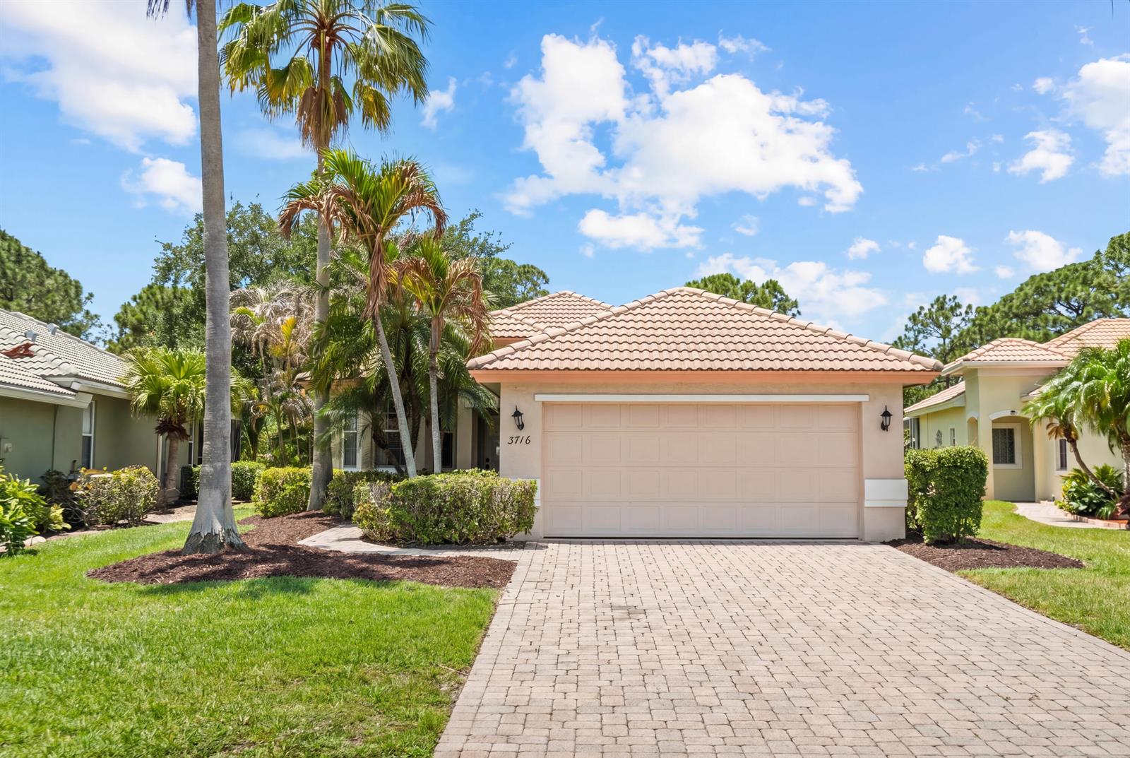 A single-story house with a beige garage, tile roof, and palm trees in the front yard — 3716 NW Deer Oak Drive, Jensen Beach FL 34957, JENSEN BEACH, FL