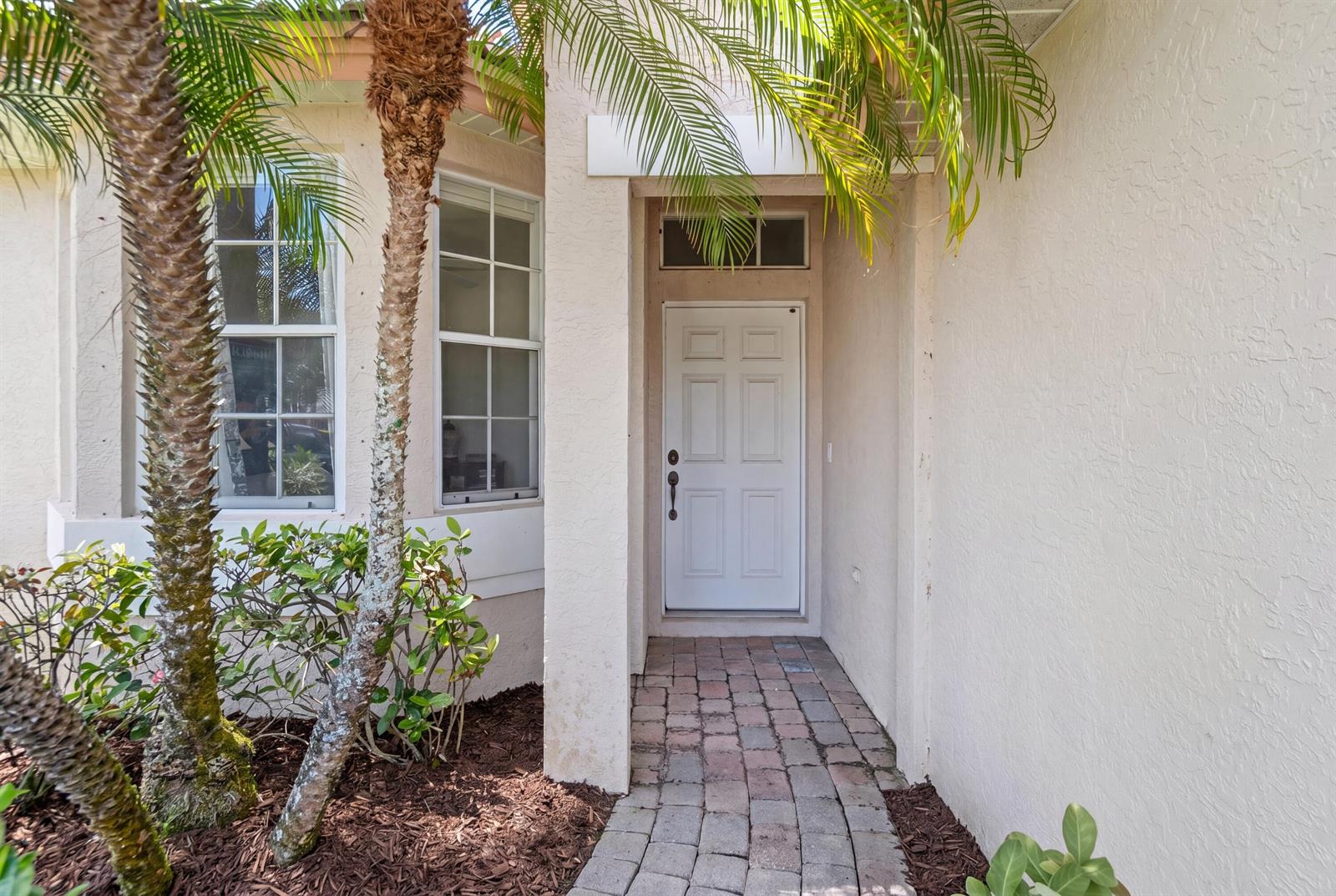 A white front door is recessed within a stucco entryway featuring a brick paver path — 3716 NW Deer Oak Drive, Jensen Beach FL 34957, JENSEN BEACH, FL