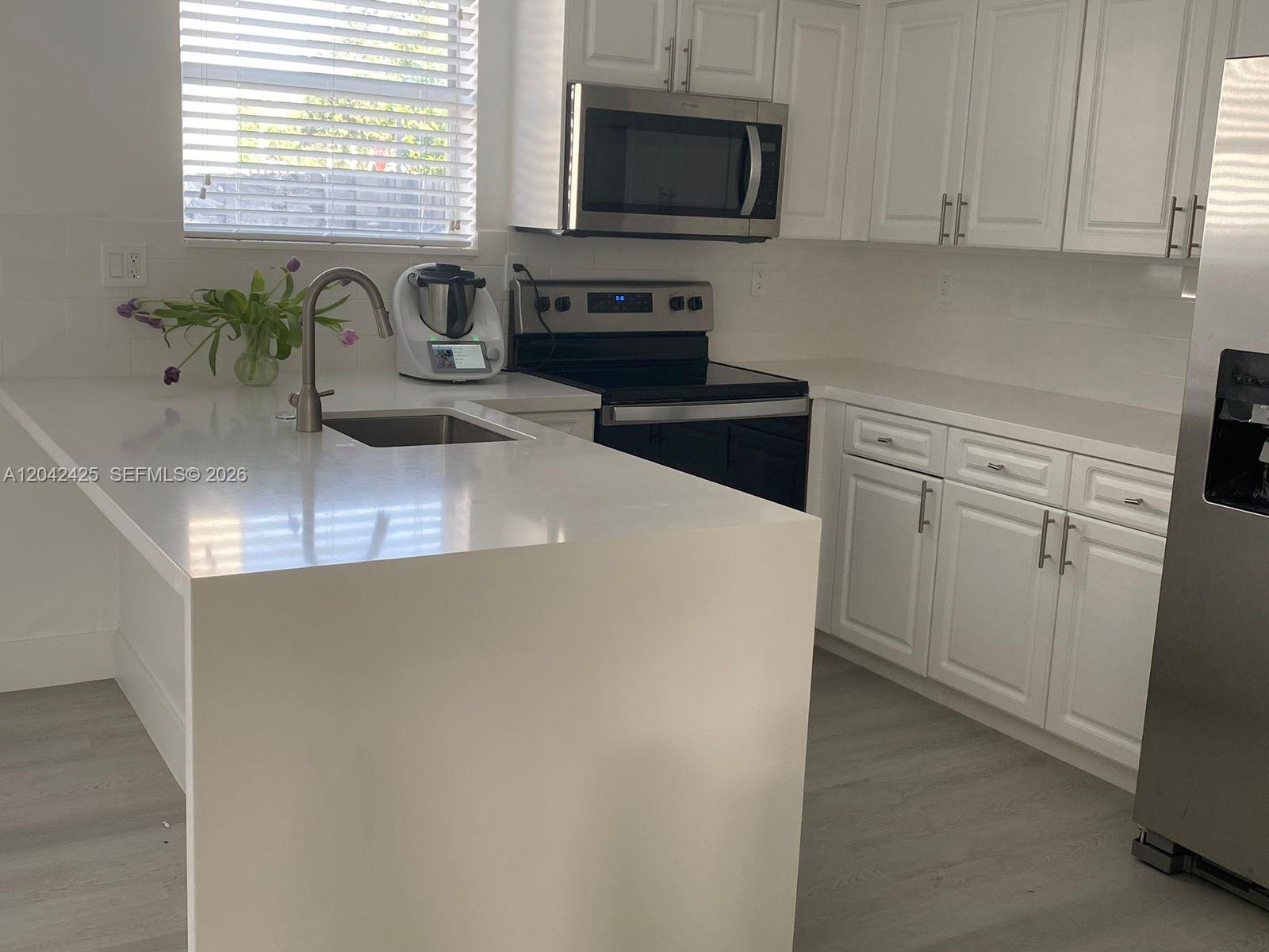 A modern kitchen features white cabinets, quartz countertops, stainless steel appliances, and light flooring — 5245 NW 112th Ave # 8, Doral FL 33178, DORAL, FL
