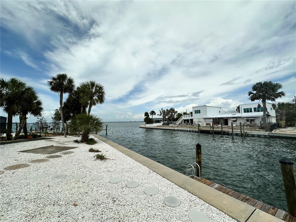 A waterfront view featuring a white gravel yard, palm trees, and a concrete seawall — 3615 100TH STREET W, BRADENTON, FL