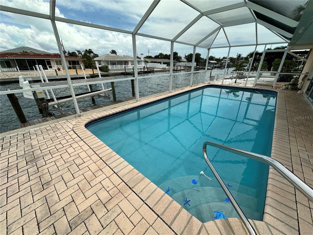 A screened-in swimming pool overlooks a canal with a boat dock and neighboring houses — 3615 100TH STREET W, BRADENTON, FL