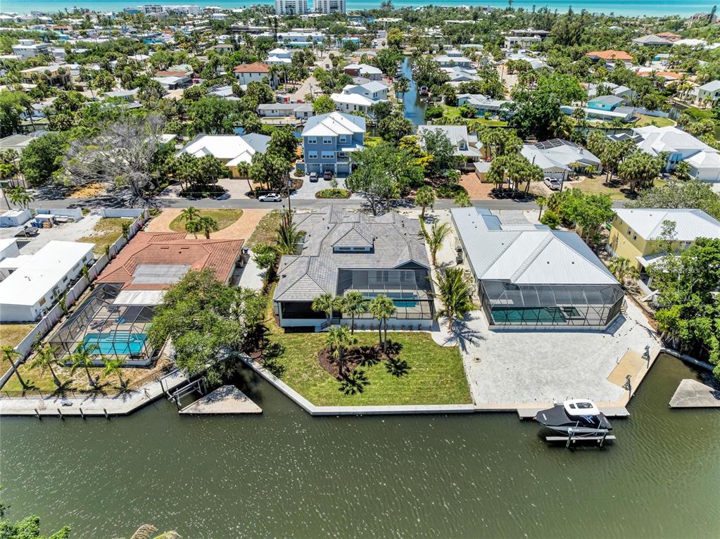 An aerial view shows three waterfront houses with pools along a canal in a neighborhood — 5103 WINDWARD AVENUE, SARASOTA, FL