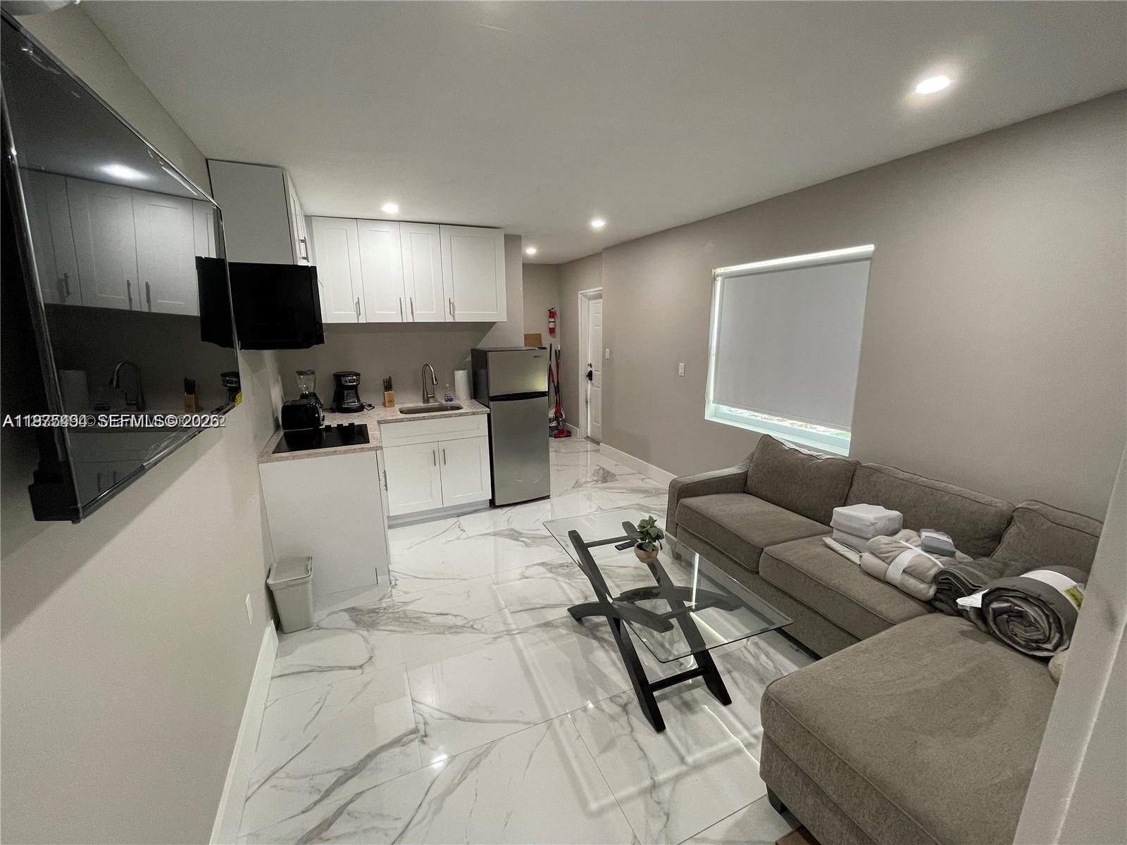 A small kitchen with white cabinets and a gray sectional sofa sit on marble floors — 4910 SW 28th Ter # 3, Dania Beach FL 33312, DANIA BEACH, FL