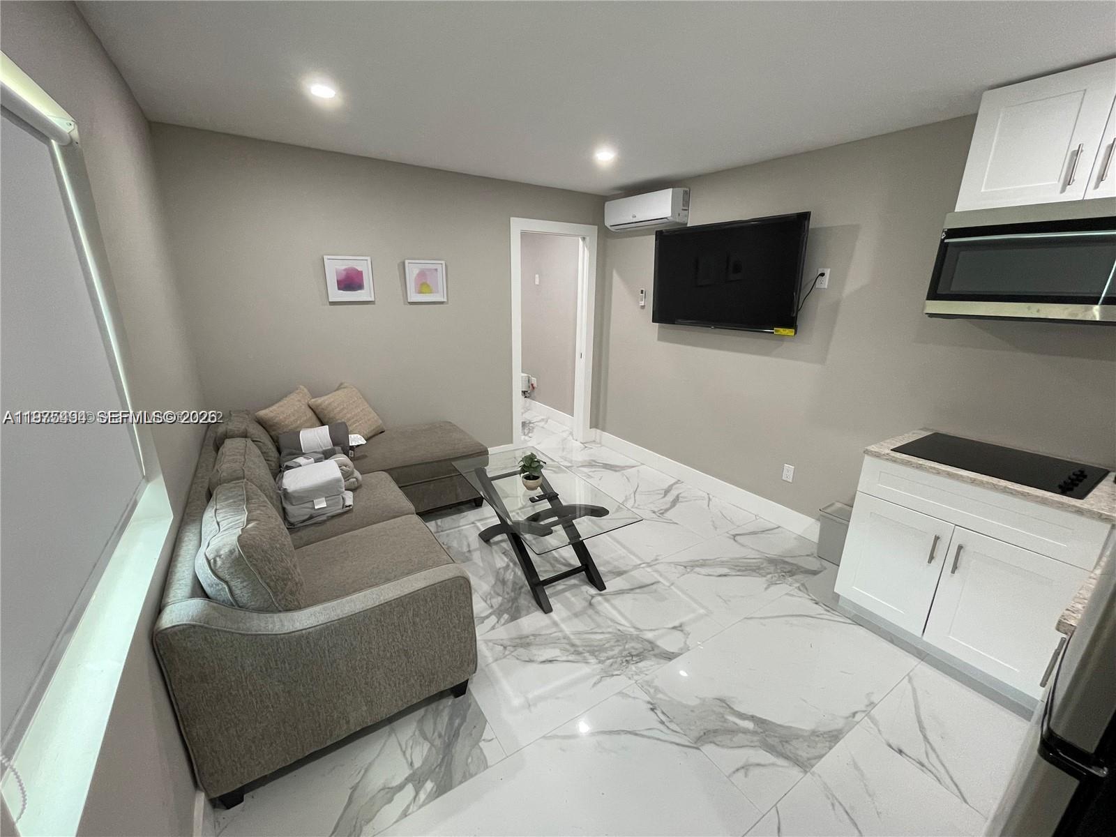 A small living room features a grey sofa, glass coffee table, and kitchenette area — 4910 SW 28th Ter # 3, Dania Beach FL 33312, DANIA BEACH, FL