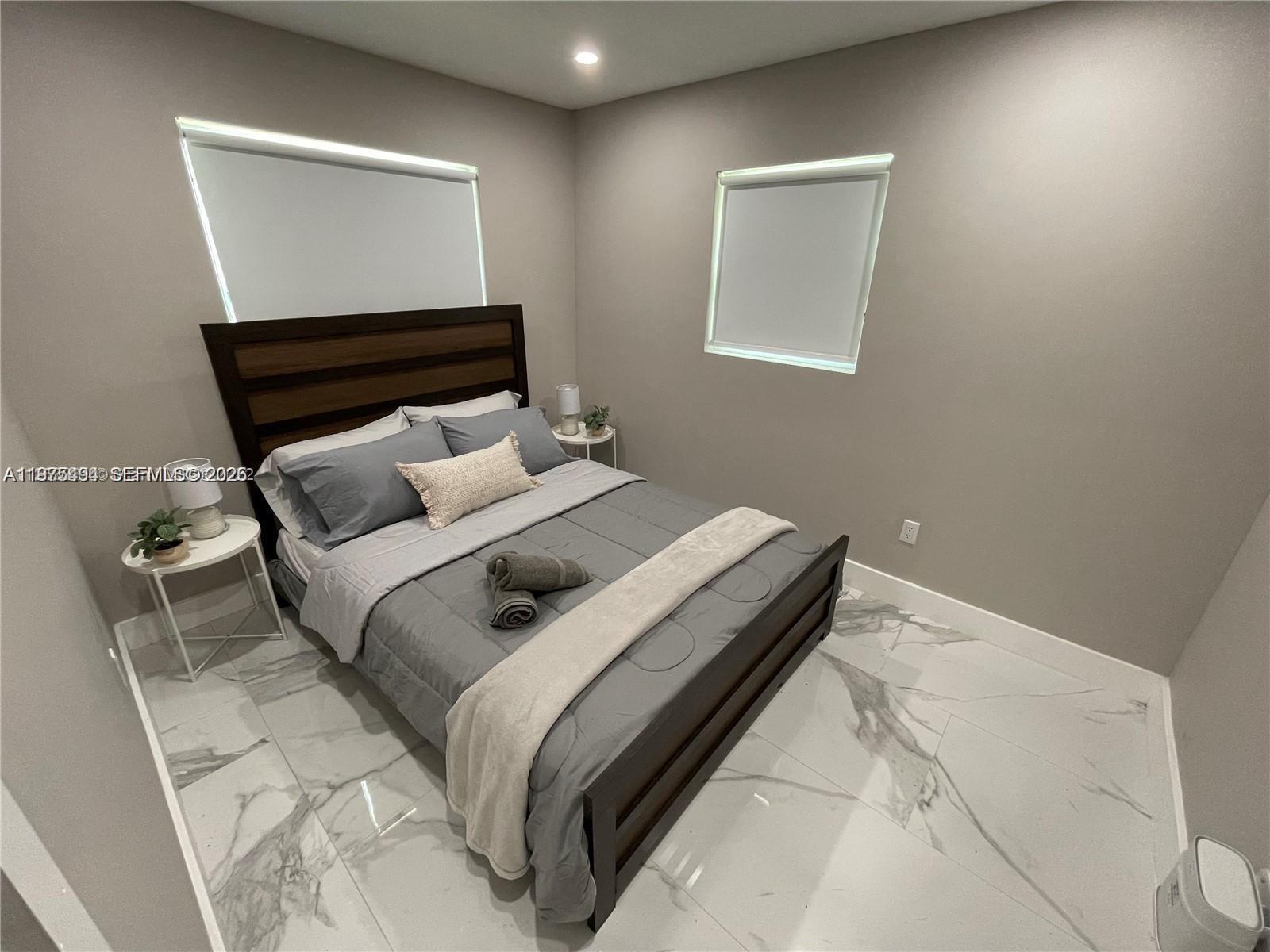A bedroom features a bed with a dark wood frame, gray bedding, and marble flooring — 4910 SW 28th Ter # 3, Dania Beach FL 33312, DANIA BEACH, FL