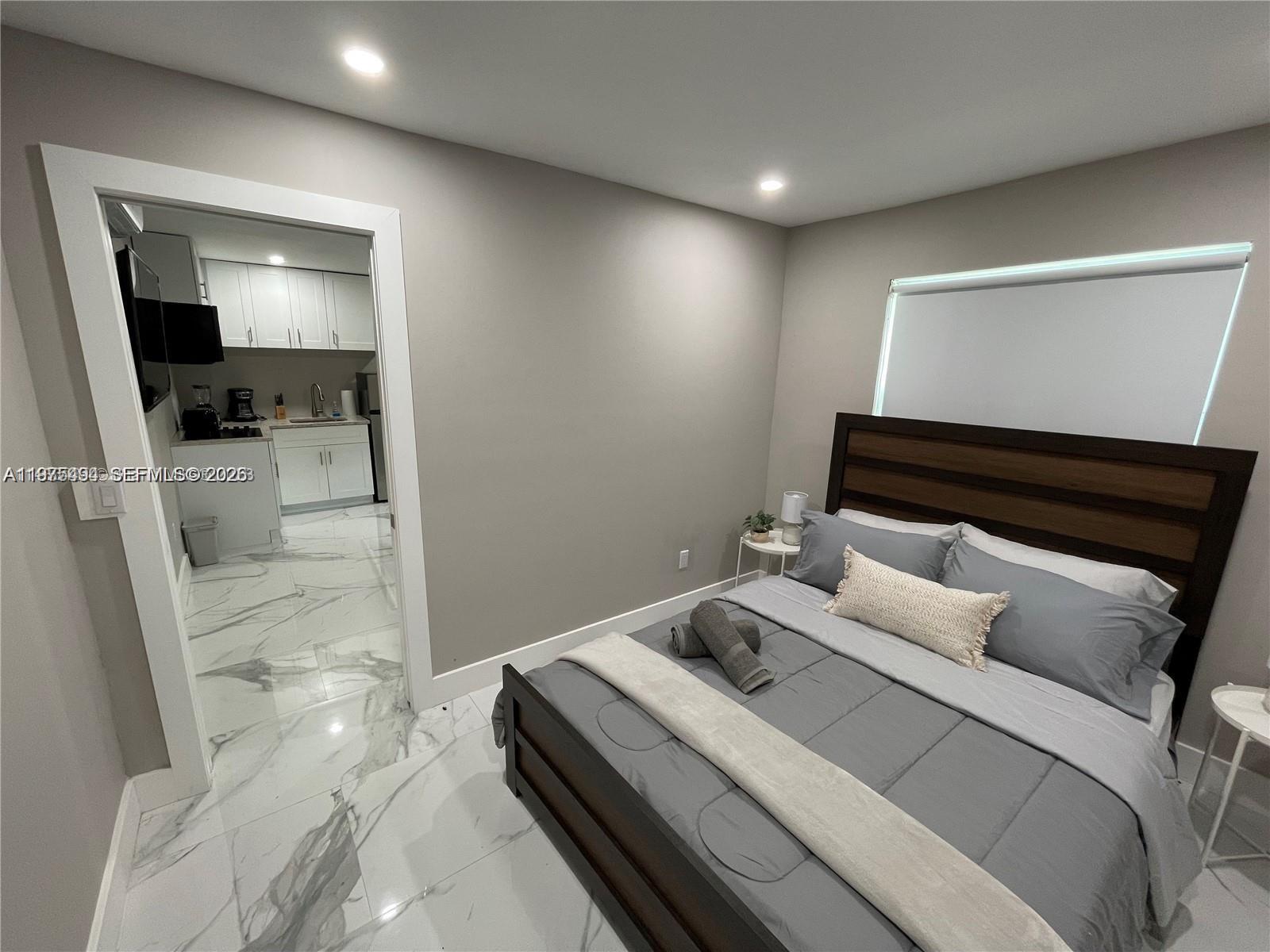 A bedroom with a dark wood bed frame and marble flooring leads into a kitchen — 4910 SW 28th Ter # 3, Dania Beach FL 33312, DANIA BEACH, FL