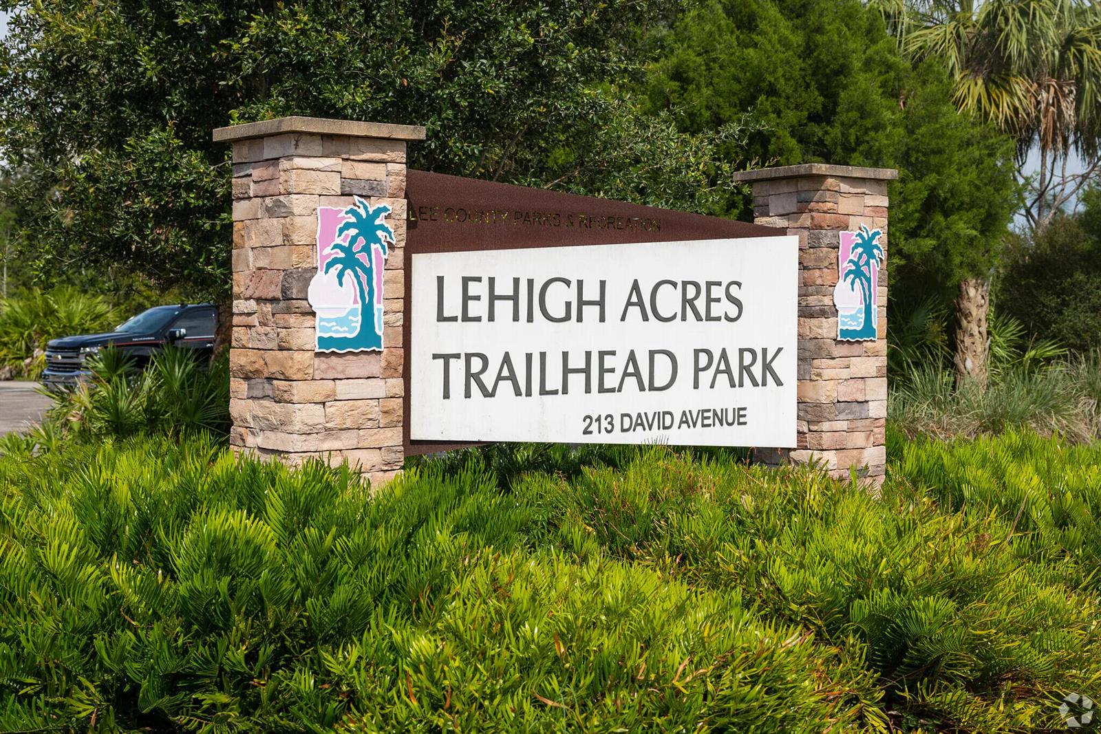 A stone-pillared sign for Lehigh Acres Trailhead Park stands amidst lush green landscaping — 1246 Cordoba Street E, Lehigh Acres FL 33974, LEHIGH ACRES, FL