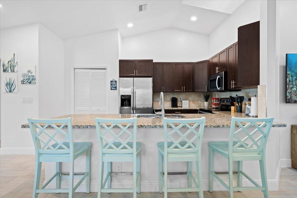 A kitchen features dark wood cabinets, granite countertops, and four light blue bar stools — 6075 Francis Street, Jupiter FL 33458, JUPITER, FL