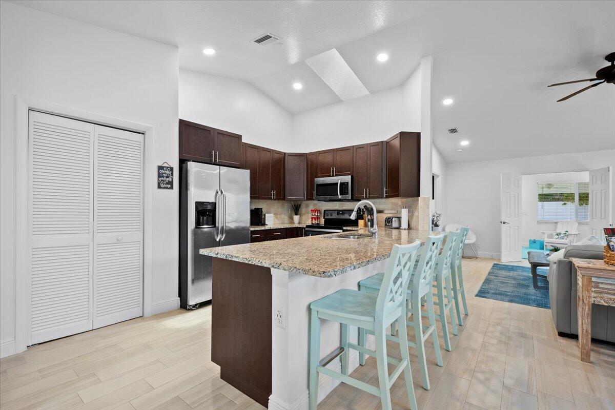 A kitchen features dark wood cabinets, granite countertops, a breakfast bar, and light-colored flooring — 6075 Francis Street, Jupiter FL 33458, JUPITER, FL