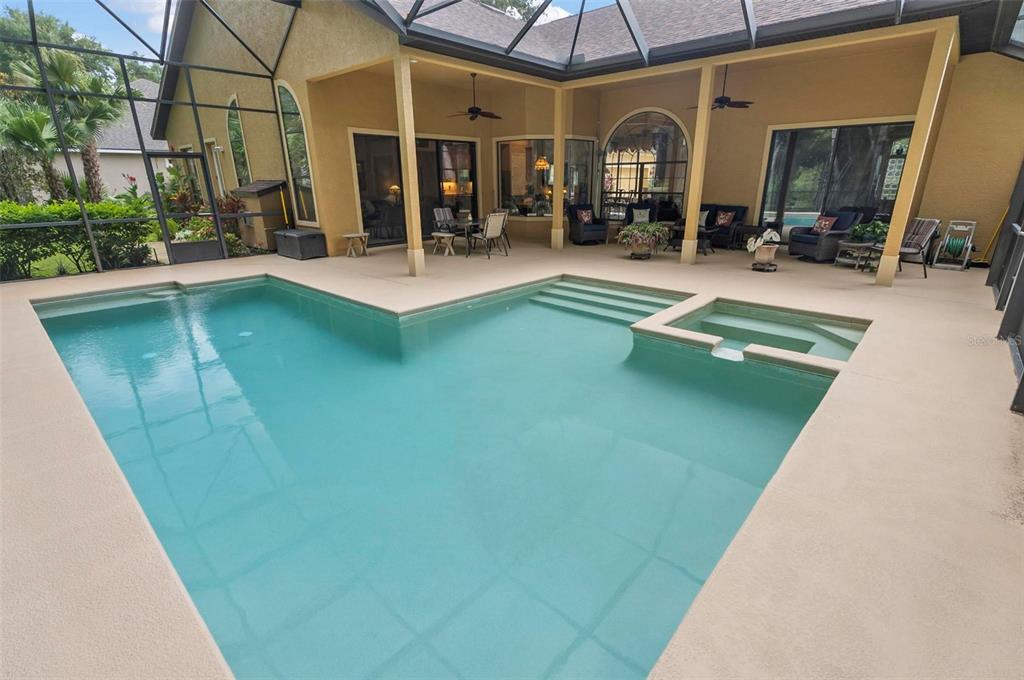 A screened-in patio features a swimming pool with an integrated spa and outdoor seating area — 23 CREEKSIDE DRIVE, PALM COAST, FL