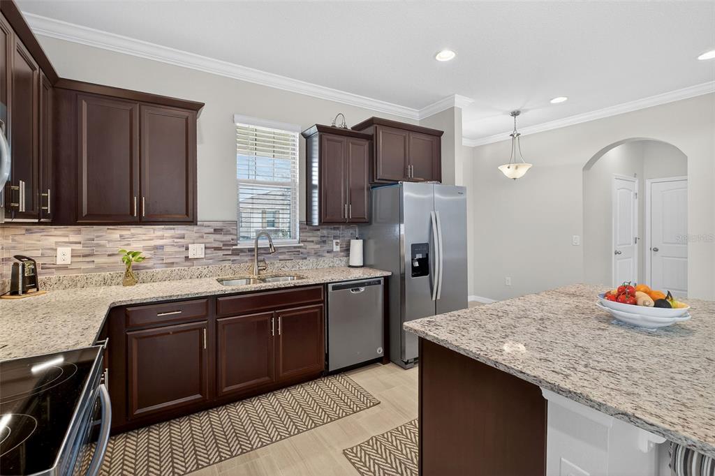 A kitchen features dark wood cabinets, granite countertops, stainless steel appliances, and a center island — 16933 OAKBORO STREET, WINTER GARDEN, FL