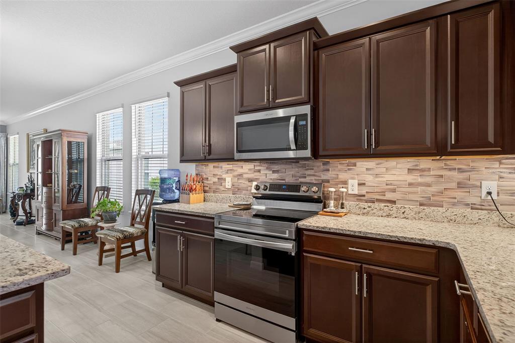 A kitchen features dark wood cabinets, granite countertops, stainless steel appliances, and a tiled backsplash — 16933 OAKBORO STREET, WINTER GARDEN, FL