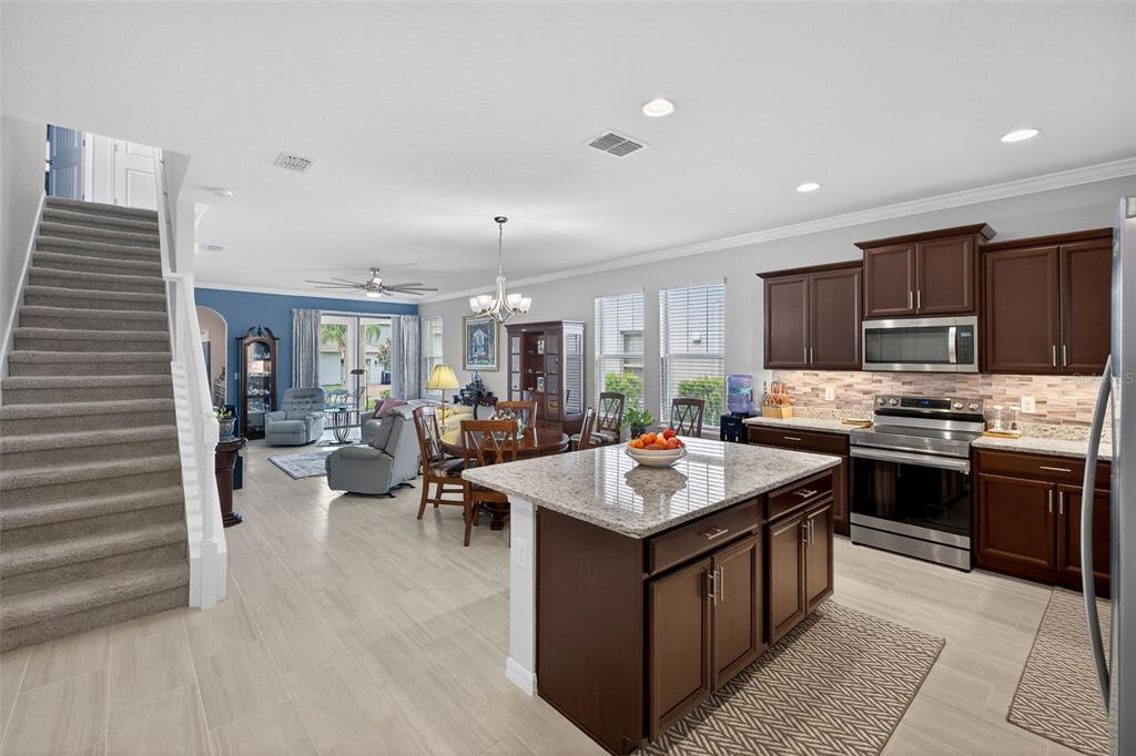 An open-concept kitchen and living area features dark wood cabinets, granite countertops, and carpeted stairs — 16933 OAKBORO STREET, WINTER GARDEN, FL
