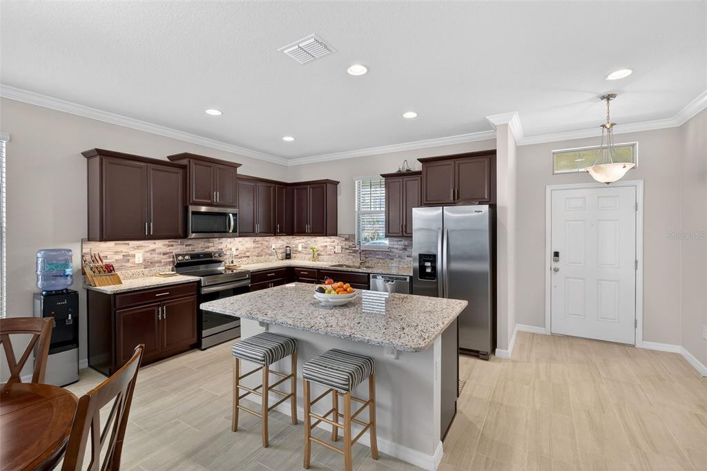 A kitchen features dark wood cabinets, granite countertops, a center island, and stainless steel appliances — 16933 OAKBORO STREET, WINTER GARDEN, FL