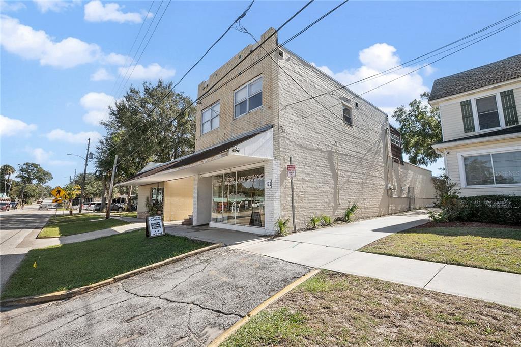 A two-story brick commercial building with a storefront window and an adjacent residential house — 128 E RICH AVENUE, DELAND, FL