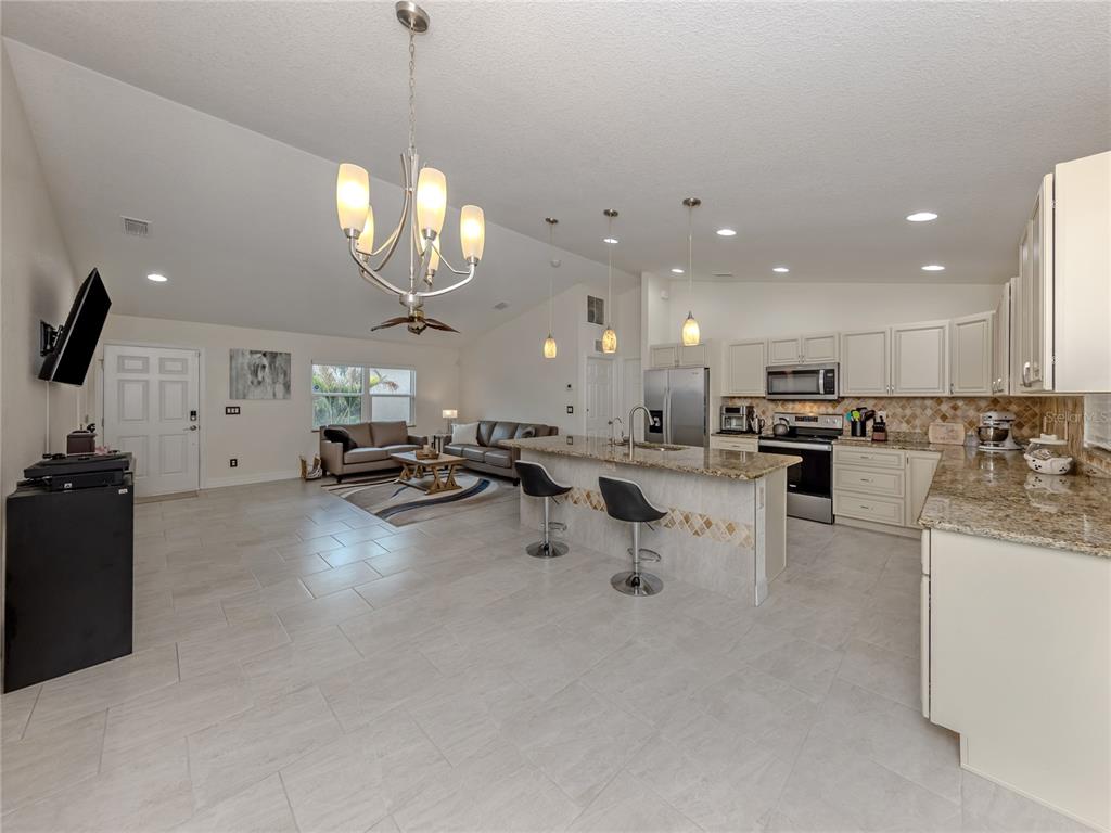 An open-concept kitchen and living area features light tile flooring, granite countertops, and vaulted ceilings — 3453 DRYDEN STREET, NORTH PORT, FL