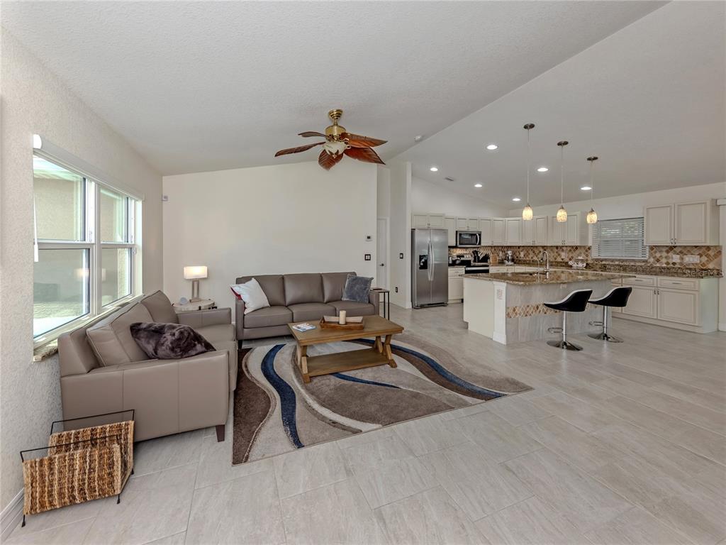 An open-concept living room and kitchen featuring tile floors, neutral cabinetry, and a ceiling fan — 3453 DRYDEN STREET, NORTH PORT, FL