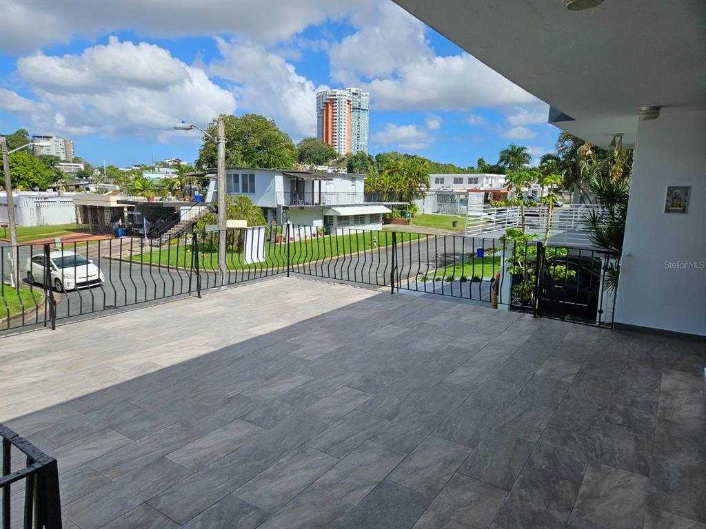 A spacious, tiled outdoor balcony features a black metal railing overlooking a residential street — 2085 Hercules st URB ALTO APOLO, GUAYNABO, PR