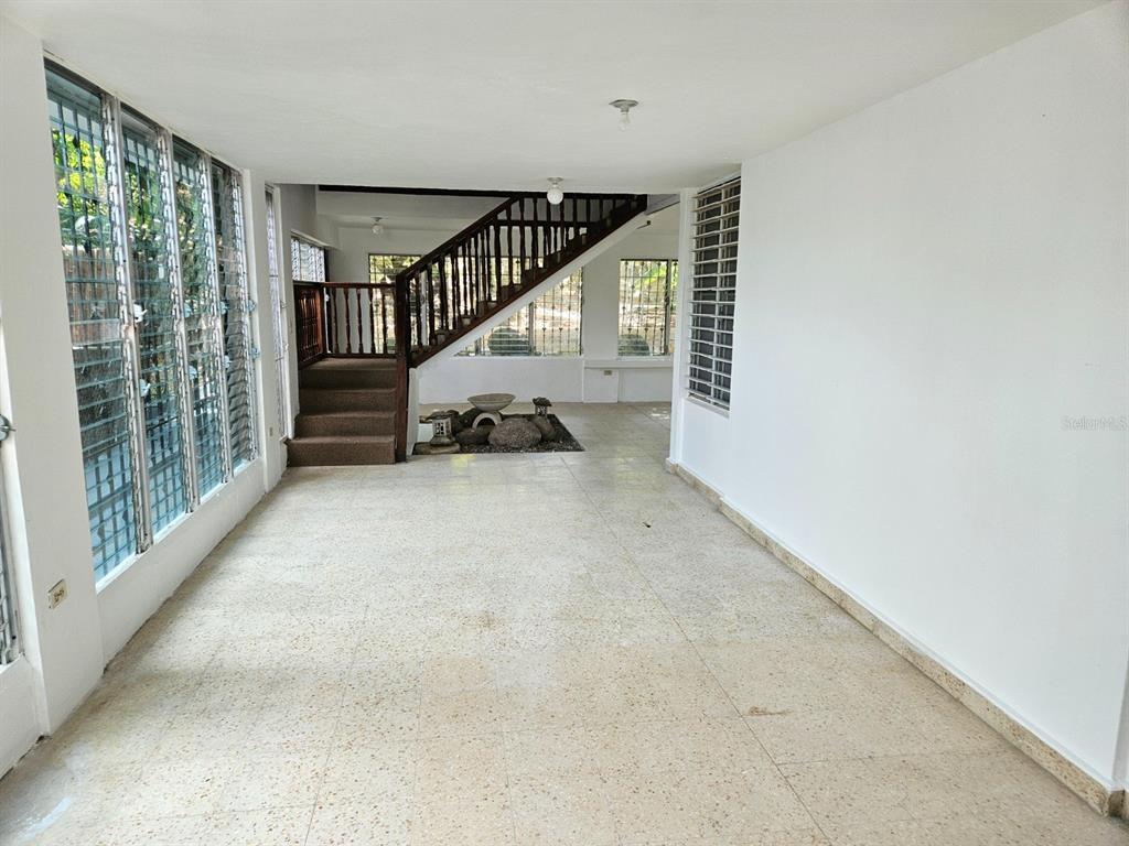 A spacious room with terrazzo floors, large windows, and a wooden staircase leading upstairs — 2085 Hercules st URB ALTO APOLO, GUAYNABO, PR