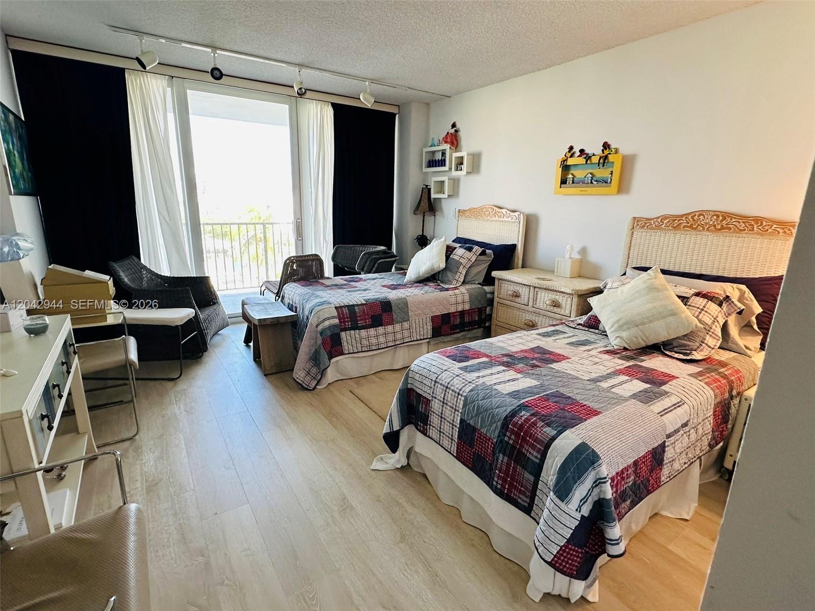 A bedroom features two beds with patchwork quilts, light wood flooring, and a balcony view — 4750 S Ocean Blvd # 401, Highland Beach FL 33487, HIGHLAND BEACH, FL