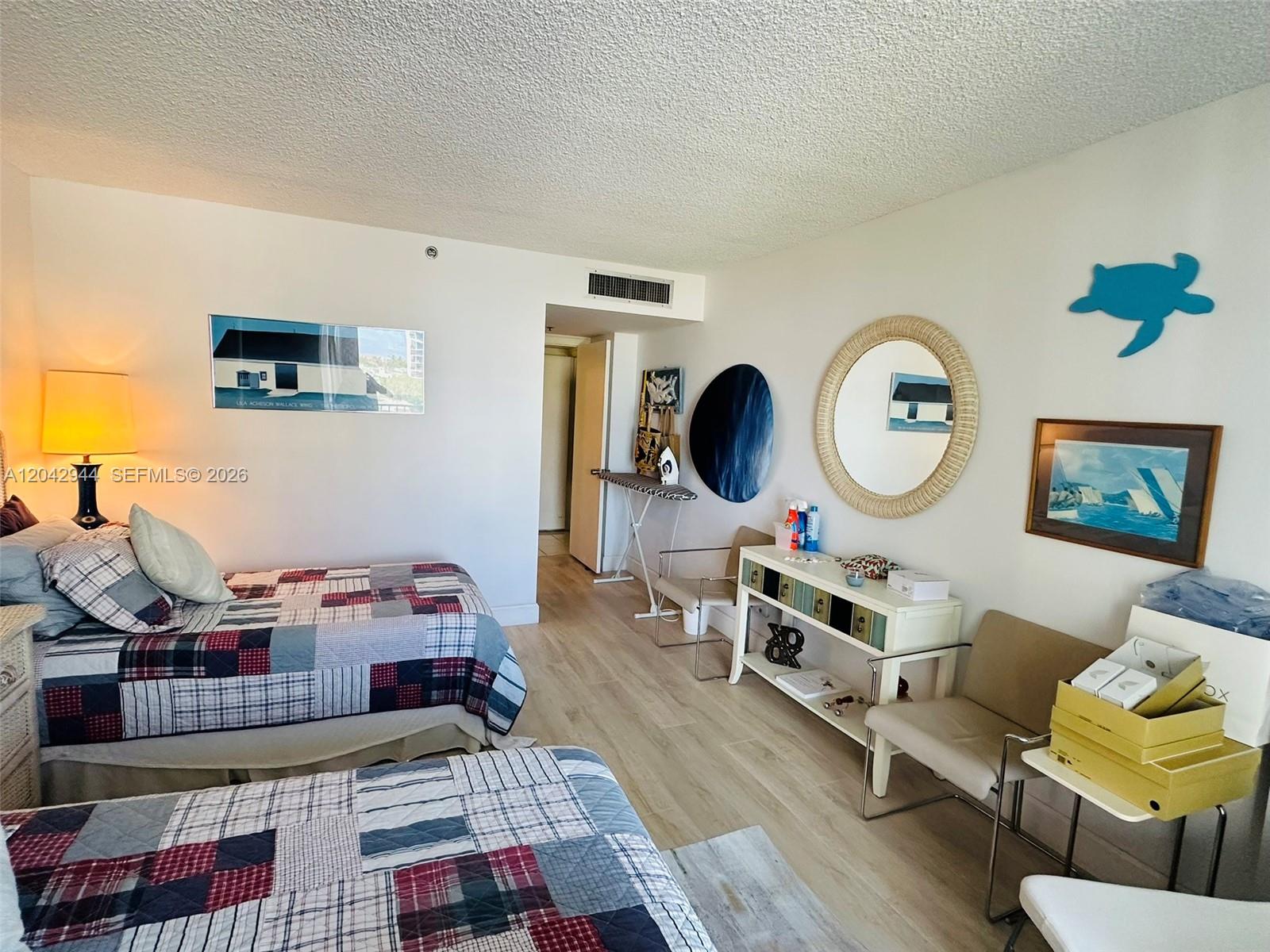 A bedroom features two beds with plaid quilts, a white console table, and a round mirror — 4750 S Ocean Blvd # 401, Highland Beach FL 33487, HIGHLAND BEACH, FL
