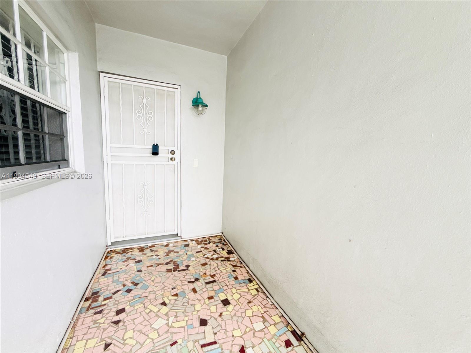A covered entryway features a white security door, a wall-mounted light, and mosaic tile flooring — 555 SW 16th Ave # 11, Miami FL 33135, MIAMI, FL